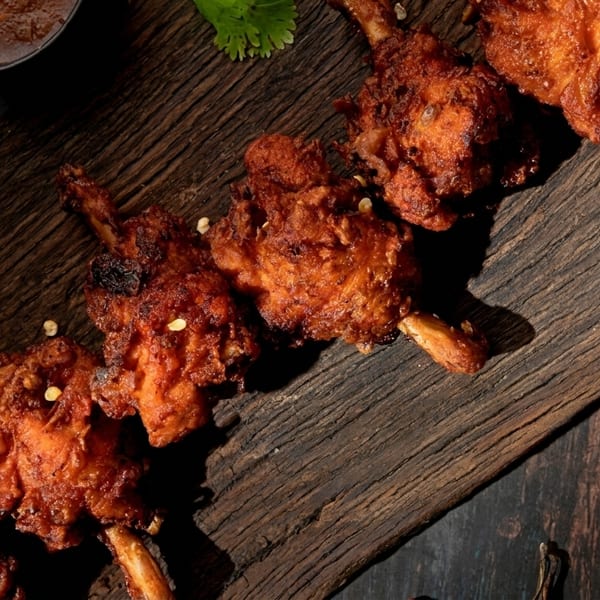 Crispy fried chicken drumettes, or lollipops, arranged on a rustic wooden board with dipping sauce.