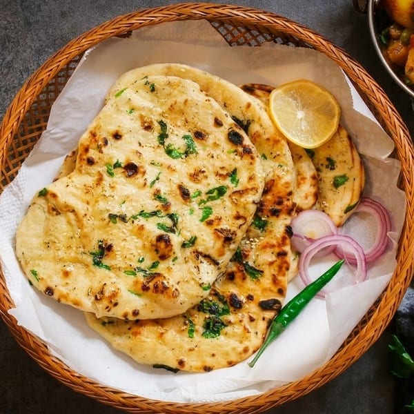Basket of naan bread with lemon, red onion, and chili, next to a bowl of potato curry.