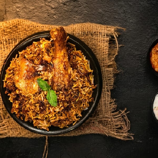 Chicken biryani with two sauces, green chilies, and spices on a dark textured surface.
