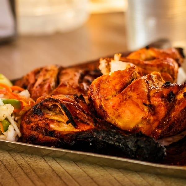 Grilled chicken pieces with crispy skin and a side of fresh vegetable salad on a silver platter.