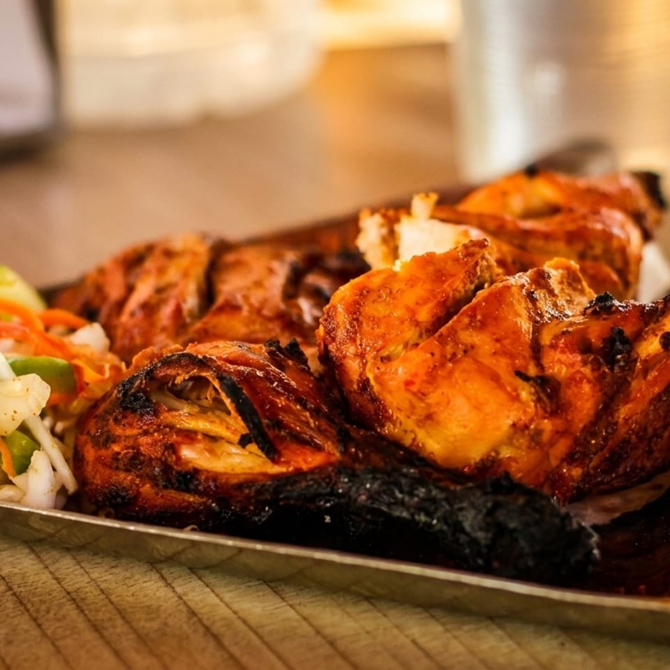Grilled chicken pieces with crispy skin and a side of fresh vegetable salad on a silver platter.